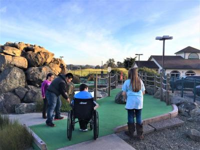 family with kid in wheelchair playing mini golf